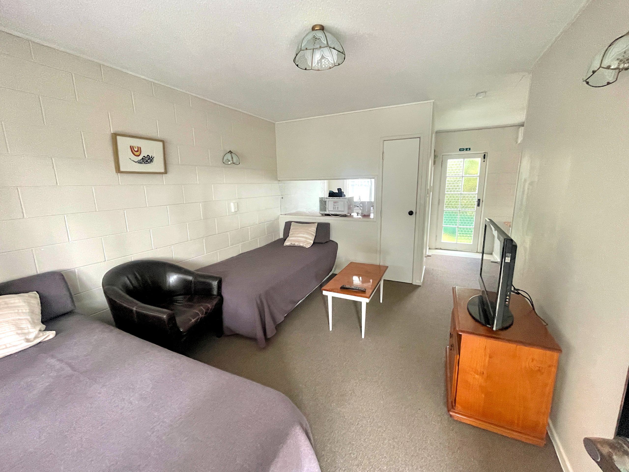 One-bedroom unit living area with beds and TV at Browns Bay Olive Tree Motel